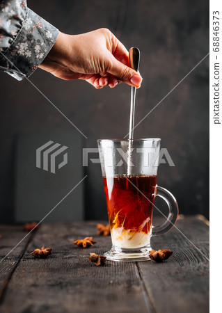 Stirring condensed milk in a glass mug with coffee Stirring condensed milk in a glass mug with coffee 68846373