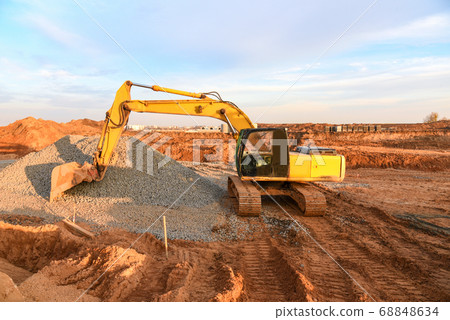 Excavator working on road work at a construction site on sunset background Excavator working on road work at a construction site on sunset background 68848634