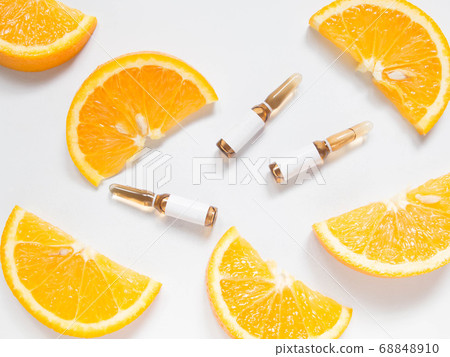 Vitamin C brown ampule for injection with fresh juicy orange fruit slides on white table. High dose vitamin c synthetic for white skin. Beauty product branding mock-up. Healthy lifestyle. Top view. 68848910