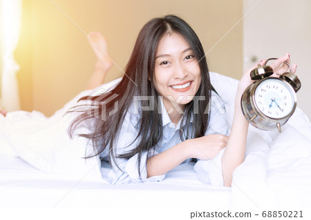 Smiling young woman on white blanket holding alarm Smiling young woman on white blanket holding alarm 68850221
