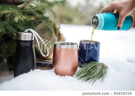 Pouring hot tea in metal thermo mugs in the snow Pouring hot tea in metal thermo mugs in the snow 68850559