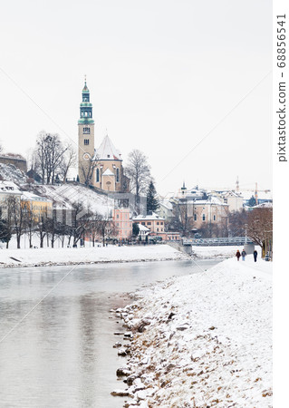 A mid winter view along the Salzach River in Salzburg, Austria. In the background can be seen the "Mullner Steg" Bridge and the parish church Mulln, a Roman Catholic church. 68856541