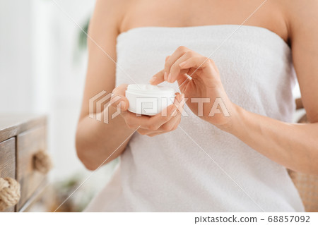 Closeup of woman wrapped in towel holding jar with cream Closeup of woman wrapped in towel holding jar with cream 68857092
