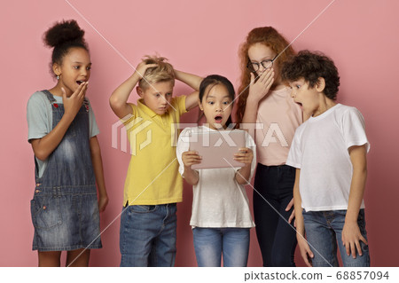Surprised boys and girls looking at tablet computer together, learning shocking news over pink background Surprised boys and girls looking at tablet computer together, learning shocking news over pink background 68857094