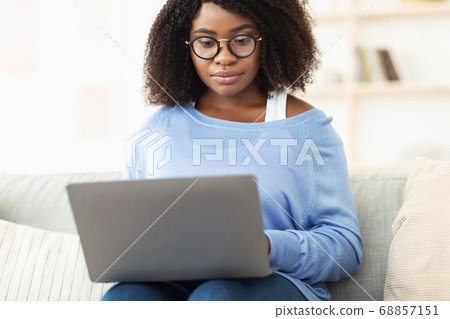 Focused black woman sitting on couch with pc Focused black woman sitting on couch with pc 68857151