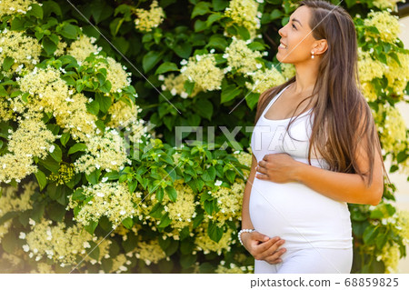 Dreamy smiling pregnant woman in beautiful garden looking at the sky 68859825