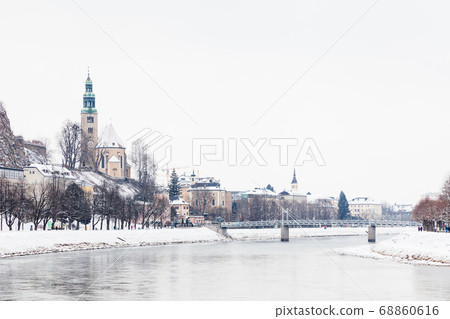 A mid winter view along the Salzach River in Salzburg, Austria looking towards the "Mullner Steg" Bridge and the parish church Mulln, a Roman Catholic church. A mid winter view along the Salzach River in Salzburg, Austria looking towards the "Mullner Steg" Bridge and the parish church Mulln, a Roman Catholic church. 68860616