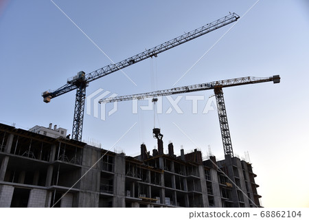 Silhouette of tower cranes constructing new residential building at construction site against sunset 68862104