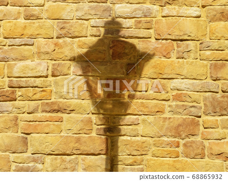 Closeup photo of an illuminated orange-yellow brick wall with a falling shadow from a lantern on it Closeup photo of an illuminated orange-yellow brick wall with a falling shadow from a lantern on it 68865932