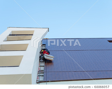 View from the bottom up on the wall of the building with an industrial climber hanging from the roof restoring a fragment of the wall View from the bottom up on the wall of the building with an industrial climber hanging from the roof restoring a fragment of the wall 68866057