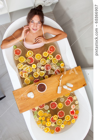 Top view of caucasian female in swimsuit sitting in bathtub with fresh slices of tropical fruits. 68866907