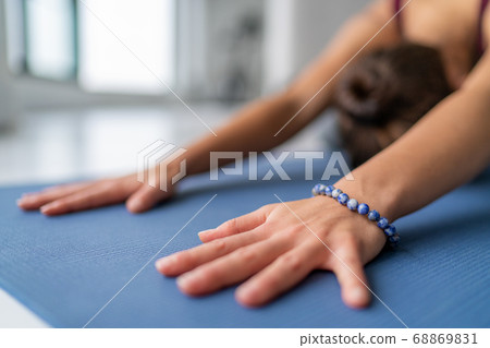 Yoga meditation woman doing childs pose stretching in gym studio or living room home. Closeup of hands touching floor exercise mat and bracelet. Fitness wellness concept 68869831