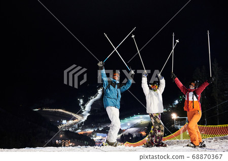 Cheerful friends skiing at ski resort at night. 68870367