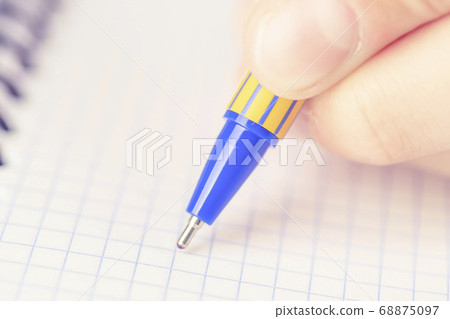 A man or teenager writes a blue-yellow pen in a checkered notebook. The concept of passing the exam and test A man or teenager writes a blue-yellow pen in a checkered notebook. The concept of passing the exam and test 68875097