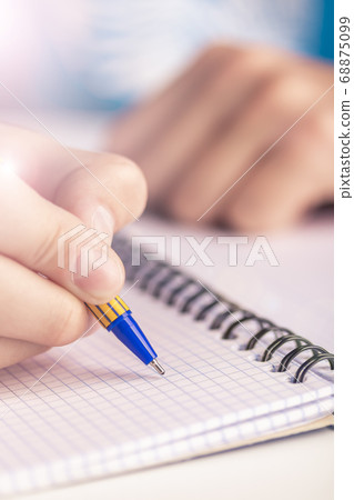 Teen writes black yellow pen in a checkered notebook. Spiral bound 68875099