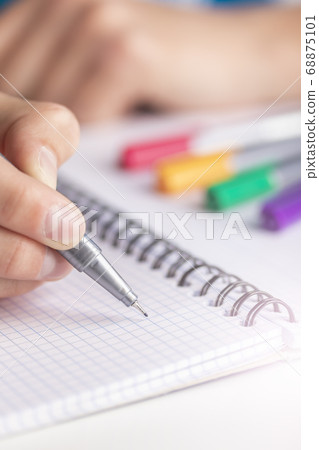 Man's hand with a black-gold pen over a clean sheet of checkered notebook. With colored markers Man's hand with a black-gold pen over a clean sheet of checkered notebook. With colored markers 68875101