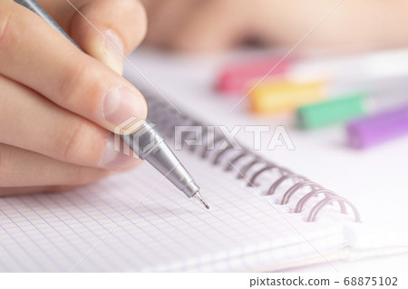 Teen writes black yellow pen in a checkered notebook. With colored markers Teen writes black yellow pen in a checkered notebook. With colored markers 68875102