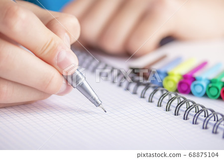 Man's hand with a black-gold pen over a clean sheet of checkered notebook. With colored markers Man's hand with a black-gold pen over a clean sheet of checkered notebook. With colored markers 68875104