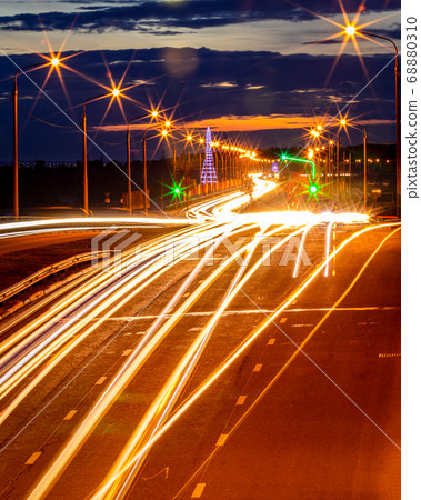 Traces of headlights from cars moving at night on the bridge, illuminated by lanterns. Abstract cityscape with highway at dusk. Traces of headlights from cars moving at night on the bridge, illuminated by lanterns. Abstract cityscape with highway at dusk. 68880310