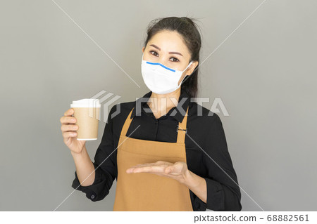 Small business owner young asian woman propose hand arm paper cups hot beverage invite visit cafe for the reopening of the place after the quarantine,wear medical face mask and brown apron Small business owner young asian woman propose hand arm paper cups hot beverage invite visit cafe for the reopening of the place after the quarantine,wear medical face mask and brown apron 68882561