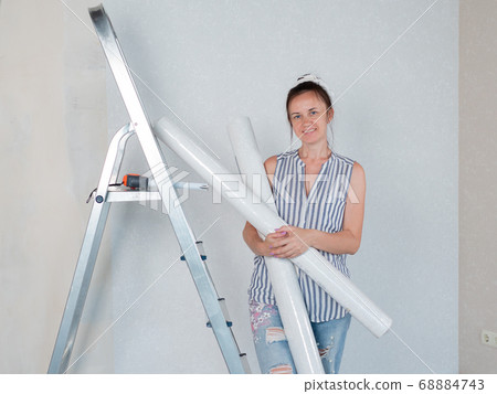 Portrait of a happy woman with rolls of Wallpaper in her hands is leaning on a stepladder. Renovation of the room. 68884743