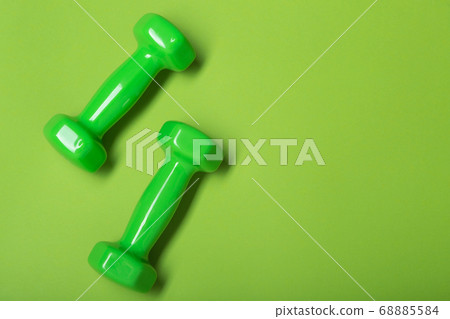 two green dumbbells on a green background, concept, copy space two green dumbbells on a green background, concept, copy space 68885584