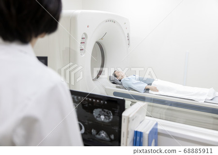 Young woman performing CT examination (view from operator room) 68885911