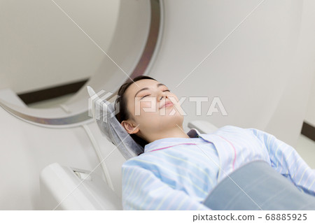 Young woman performing CT examination (view from operator room) 68885925