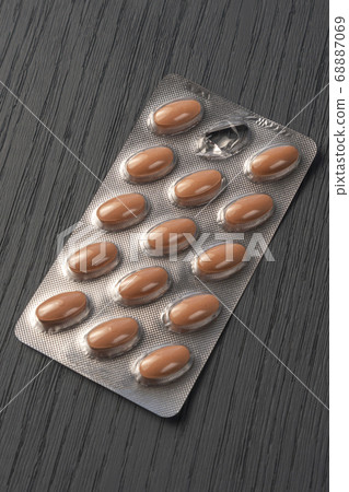 Close-up of packaging brown pills on a beautiful gray wooden textured background. One pill is missing 68887069