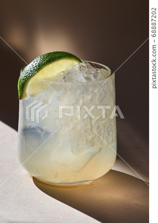Cold cocktail with lime, lemon, tonic, vodka and ice on an orange background, daylight 68887202