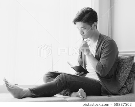 Young Asian man writing in a book when using 68887502