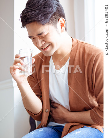 An adult sick man in a shirt with a glass of water and holds his hand on his stomach. An adult sick man in a shirt with a glass of water and holds his hand on his stomach. 68893401