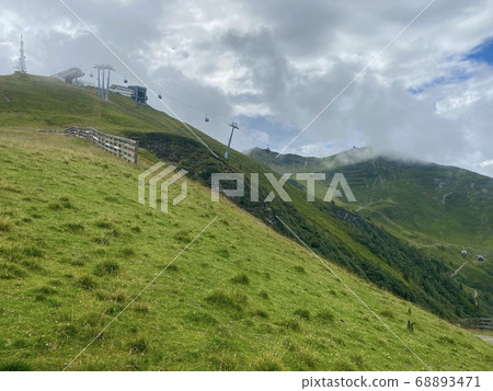 View on Schattnerg mountain station in Hinterglemm in the Austrian Alps in summer with great mountain panorama in the background and lush meadows against a cloudy sky View on Schattnerg mountain station in Hinterglemm in the Austrian Alps in summer with great mountain panorama in the background and lush meadows against a cloudy sky 68893471