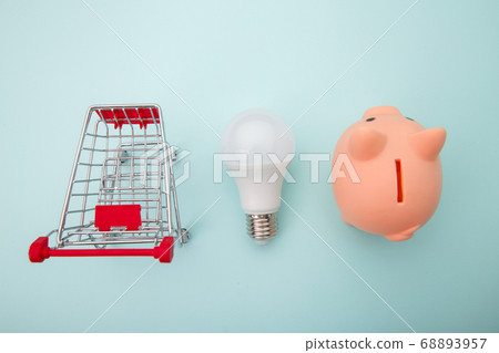 Piggy bank with trolley and lamp on blue background. Power savings concept. Top view 68893957