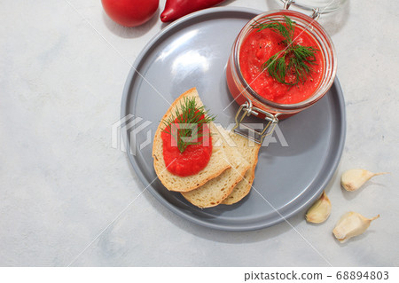 Ajvar, pepper mousse in a jar and on gray plate and gray backgground Ajvar, pepper mousse in a jar and on gray plate and gray backgground 68894803
