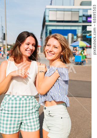 Two young girls friends walk in city in summer day Two young girls friends walk in city in summer day 68895503