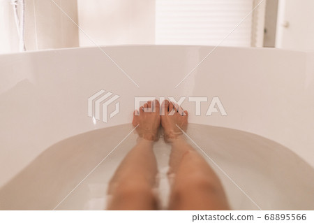Woman taking a hot bath selfie in tub home cozy relaxation in winter night. POV of feet and legs in water Woman taking a hot bath selfie in tub home cozy relaxation in winter night. POV of feet and legs in water 68895566