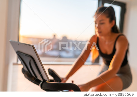 Home fitness fit woman exercising on smart stationary bike at home gym class watching screen online class biking exercise. Young girl training spinning the pedals pedaling. Focus on screen 68895569