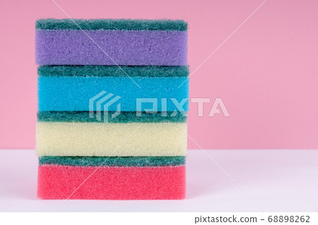Multicolored sponges for washing dishes on top of each other on a pink background. Cleaning concept. Multicolored sponges for washing dishes on top of each other on a pink background. Cleaning concept. 68898262