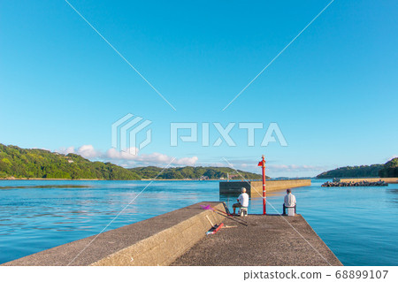 Two men enjoying fishing Two men fishing while sitting on a breakwater 68899107