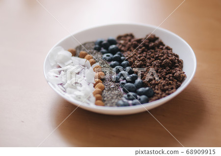 Fresh smoothie bowl with blueberry, chia seeds, almonds, coconut flakes and chocolate flakes. Morning breakfast on wooden table. Lactose free yogurt 68909915