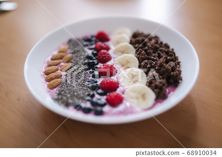 Smoothie bowl with fresh raspberry, blueberry, chia seeds, almonds, banana, and chocolate flakes. Morning breakfast on wooden table 68910034