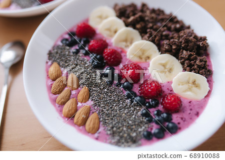 Smoothie bowl with fresh raspberry, blueberry, chia seeds, almonds, banana, and chocolate flakes. Morning breakfast on wooden table. Close up 68910088