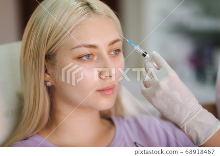 Hands of cosmetologist making injection in face, lips. Young woman gets beauty facial injections in medical clinic 68918467