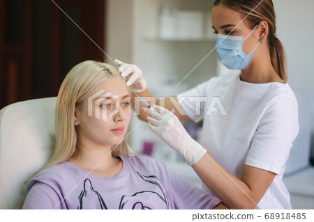 Hands of cosmetologist making injection in face, lips. Young woman gets beauty facial injections in medical clinic Hands of cosmetologist making injection in face, lips. Young woman gets beauty facial injections in medical clinic 68918485