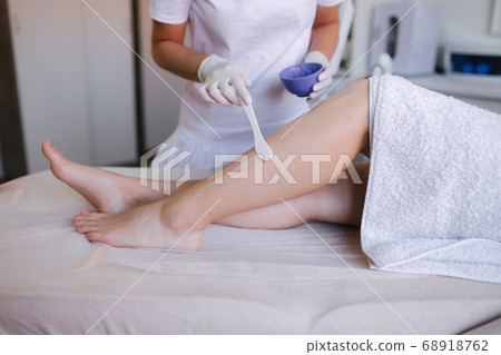 Young woman beautician in mask applies contact gel on the leg of a woman for laser hair removal in medical clinic. Close up Young woman beautician in mask applies contact gel on the leg of a woman for laser hair removal in medical clinic. Close up 68918762