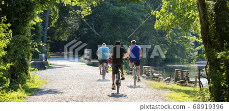 Three men riding bicycles on trail passing a lake 68919396