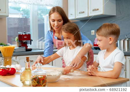 Mother and her little kids, boy and girl, helping her to prepare dough 68921192