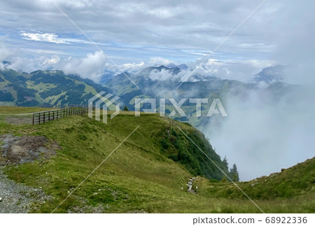 View towards the mountains in Saalbach-Hinterglemm skiing region in Austria on a beautiful summer day with low hanging clouds and lush meadows used by cows for grazing 68922336