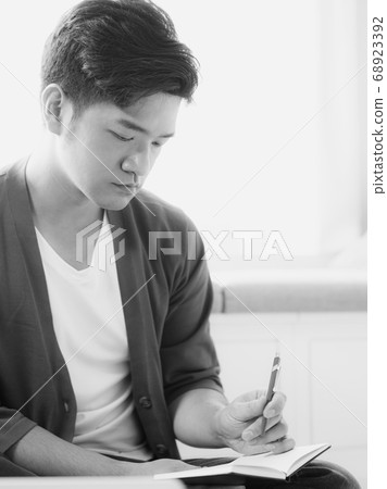 Young asian man writing in notebook. Young asian man writing in notebook. 68923392